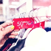 donna negozio saldi una donna in un negozio di abbigliamento guarda un cartellina che indica il 50% di sconto