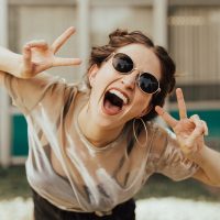 donna felice una ragazza con gli occhiali da sole sorride e fa il segno della vittoria